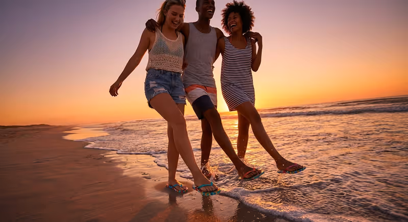 Friends in stylish flip flops walking along the shoreline at sunset